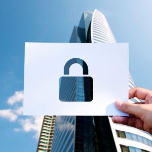 Papier perforé avec cadenas devant un immeuble de bureaux illustrant la protection des entreprises par des droits de propriété intellectuelle