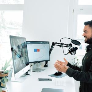 Man maakt webcast voor een staand bureau met een professionele microfoonset en twee grote computerschermen
