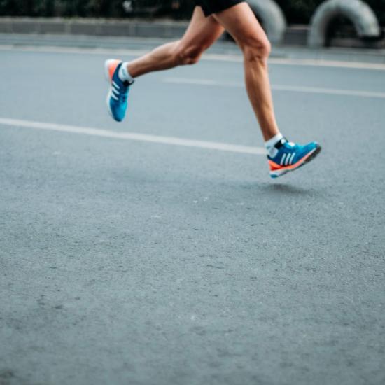 Hardloper met blote benen en heldere blauwe hardloopschoenen rennende op een asfaltweg  ter illustratie van bewegingsanalyse van de plantaire druk van de voet bij loopoefeningen