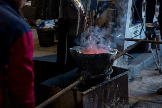 Metaal wordt gegoten in een gietpan in een industriële omgeving, met rook en gloeiende hitte. Illustratie van vuurvaste bekledingen bij gietpannen en inductieovens.