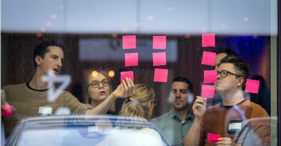 People in a brainstorm, looking at post-its on a window. 