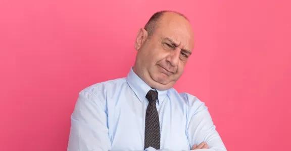 Confident business professional in a light blue shirt and tie with arms crossed, standing against a bright pink background, symbolizing assertiveness and determination in leadership for circular project success.