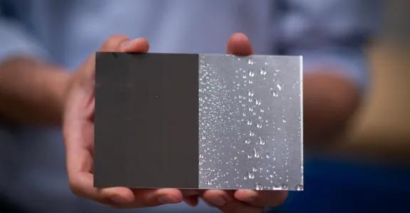 Close-up of a metal plate textured by laser technology, showing a textured hydrophobic surface on one side and a plain untreated side. Demonstrates the functional properties of femtosecond laser texturing.