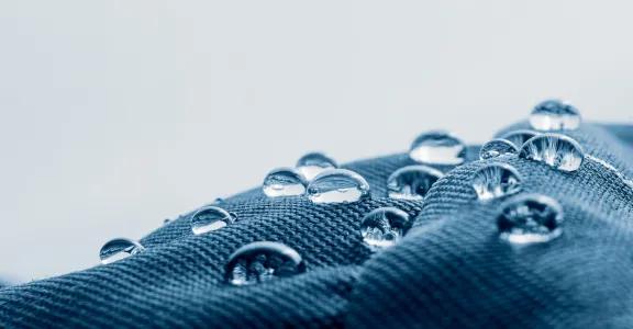 Close-up of water droplets on a hydrophobic and oleophobic textile surface, illustrating the goal of the BIOSUPHYOL industrial research project on bio-based and PFAS-free coatings.