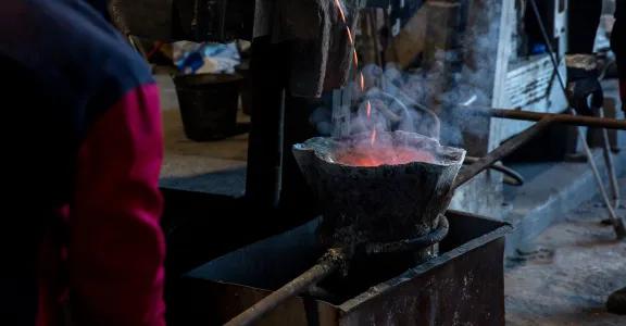 Metaal wordt gegoten in een gietpan in een industriële omgeving, met rook en gloeiende hitte. Illustratie van vuurvaste bekledingen bij gietpannen en inductieovens.