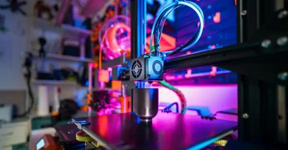 Een 3D-printer in actie, met gekleurde lichtjes op de  achtergrond. ter illustratie van elektrificatie en additive manufacturing als geavanceerde technologieën in productieprocessen.