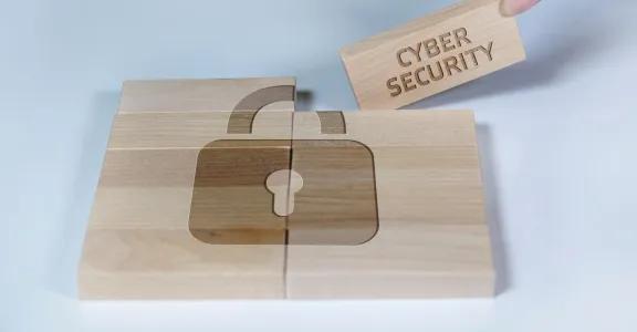 A wooden puzzle with a padlock symbol engraved on its pieces, symbolizing cybersecurity in wood production. One piece labeled "CYBER SECURITY" is being placed to complete the puzzle.