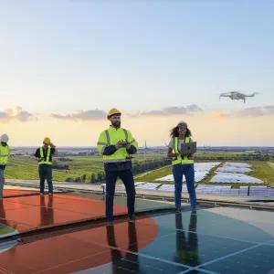 Engineers on a solar panel roof using drones and advanced technology, representing sustainable practices and innovation for the Factory of the Future.