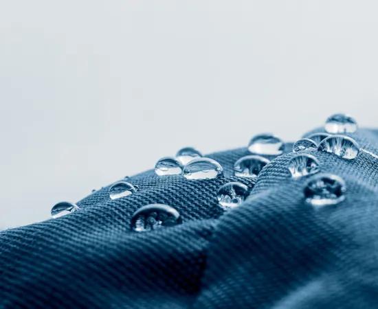 Close-up van waterdruppels op een hydrofobe en oleofobe textieloppervlakte, illustrerend het doel van het BIOSUPHYOL-industrieel onderzoeksproject naar biogebaseerde en PFAS-vrije coatings.