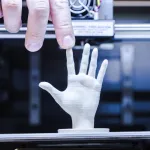 Male hand touching finger of 3D printed hand under D o