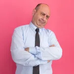 Confident business professional in a light blue shirt and tie with arms crossed, standing against a bright pink background, symbolizing assertiveness and determination in leadership for circular project success.