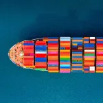 Bird view of a freighter with colourful containers referring to the business crisis due to the blocking of the Suez Canal by the container ship Ever Given and representing business resilience trough circular collaboration.